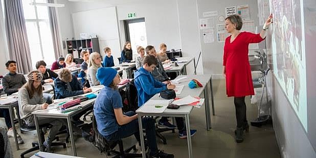 Lærer står foran en klasse, mens hun peker på tavlen. Foto.