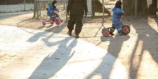 Skygger i barnehage, to barn på sykler og en voksen. Foto. 