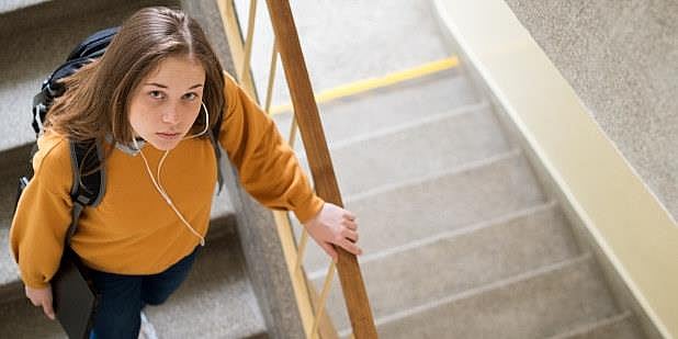 Kvinne med trist uttrykk går ned trapp i skolebygg mens hun ser opp på fotografen. Illustrasjonsfoto