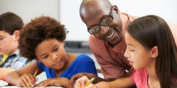 En lærer hjelper to elever ved pulten deres i klasserommet. Illustrasjonsfoto: Mostphotos