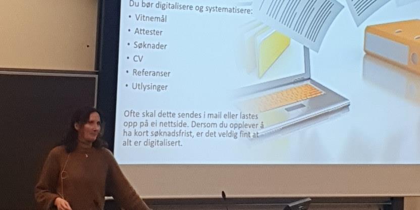 Bilde av Jill Johansen ved siden av en skjerm med en presentasjon om hva en bør digitalisere og systematisere i en søknad