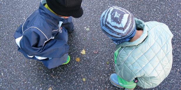To små barn som sitter på huk ute og ser på noe på asfalten.