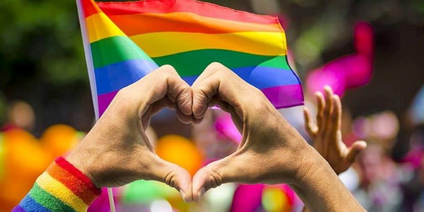 Prideflagg og to hender former et hjerte