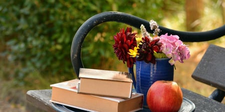 Bilde av en benk med bøker, eple og en blomstervase