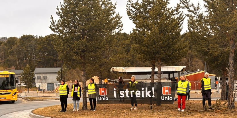 streikende Uniomedlemmer markerer ved å stå i rundkjøring i Karasjok med banner der det står Unio i streik. Noen har gule Uniovester med påtrykk streikevakt og noen viser sort skjorte med Uniotrykk.