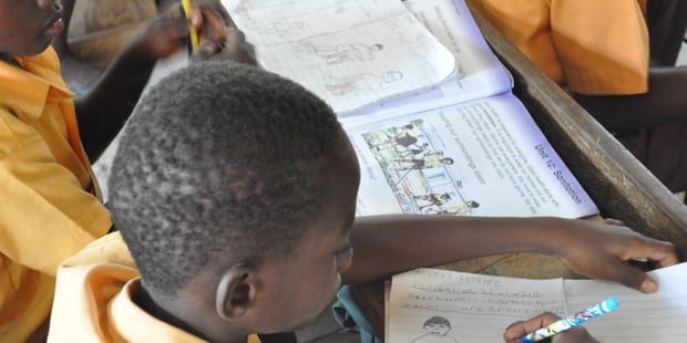 Elev ved afrikansk skole skriver i bok. Foto.