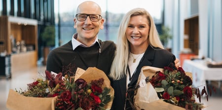 Mann og kvinne står med blomsterbukett i hendene og ser smilende mot fotografen