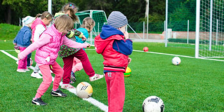 Barn leker på en fotballbane med fotballer