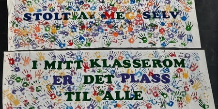 Et stofftrykk med mange barnehender og teksten "Stolt av meg selv" og
"I mitt klasserom er det plass til alle"