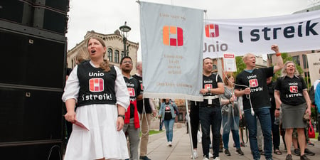 Guro Lind i forgrunnen, med streikende i tskjorter og banneret med Unio i Streik