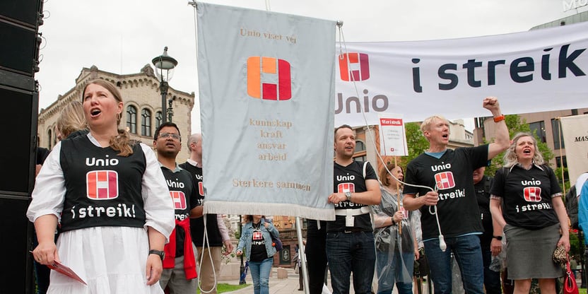 Guro Lind i forgrunnen, med streikende i tskjorter og banneret med Unio i Streik