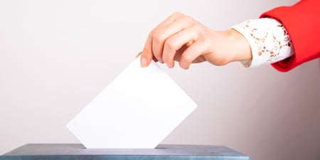 Bildet viser en hånd som dytter en stemmeseddel ned i en urne.