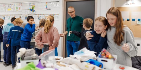 Bildet viser elever ved Oksenøya barneskole, 1. og 6. klasse i 2024. Mange elever vasker hendene, mens læreren gir instruksjoner inne i håndarbeidssalen.