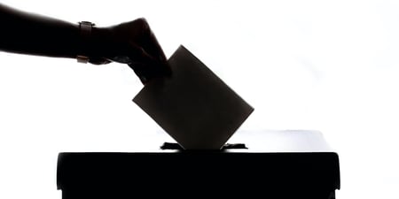 Hånd som legger en stemmeseddel ned i en stemmeboks