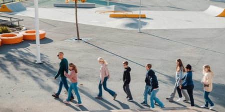 Bildet viser elever ved Oksenøya barneskole. Det er tatt ute, hvor en rekke elever marsjerer bak læreren sin.