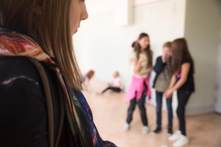 Tre jenter står sammen og hvisker mens en annen jente står lengre unna og deltar ikke