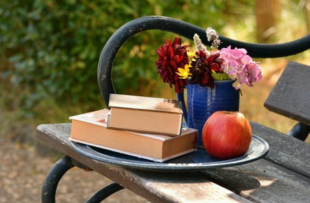 Bilde av en benk med bøker, eple og en blomstervase
