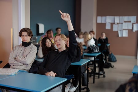 Foto av elev som rekker opp hånd i klasserom