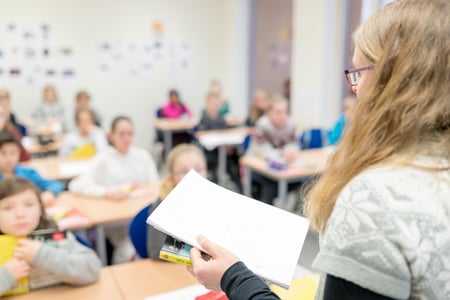 Bildet viser en kvinnelig lære bakfra. Hun står foran noen få elever i et klasserom.