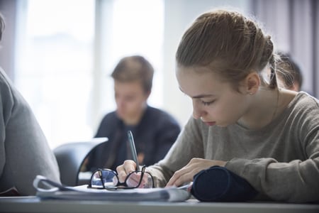 Jente skriver på et papir på en pult