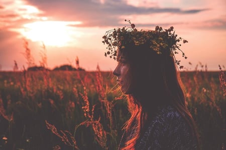 Profilbilde av en person (kvinne ) med blomsterkrans i håret. Ser solnedgangen i bakgrunnen. Illustrasjonsbilde