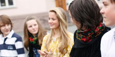 En lærer og fire elever i samtale i en skolegård. Foto.