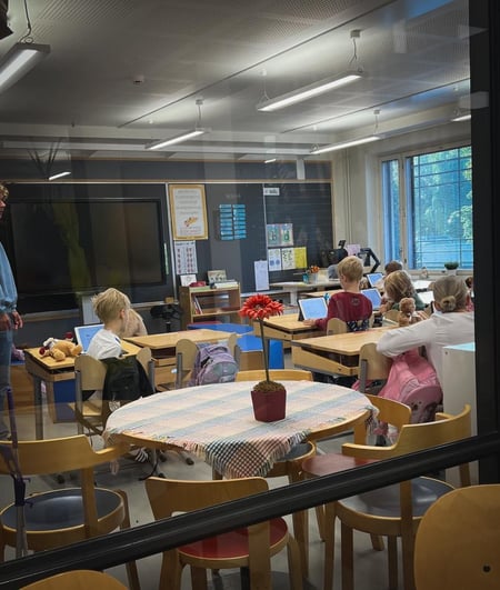 Vi ser inn gjennom vinduet til et finsk klasserom. Elever i første klasse sitter med ryggen til og skriver på PC. 