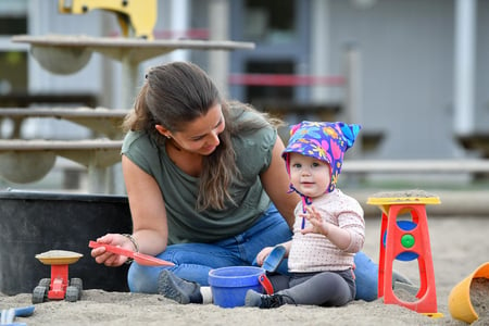 Kvinnelig barnehagelærer som er sammen med et barn i sandkassen. Foto