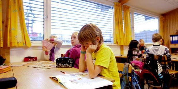 En ung elev som sitter med hodet i hendene ved en skolepult. Foto.