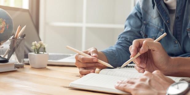 To par hender som holder blyanter over en notatblokk. Foto.