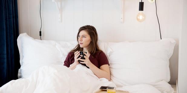 Dame i sengen med kaffekopp. Foto