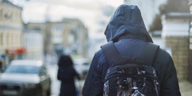 En tenåringsgutt med sekk på ryggen sett bakfra med jakkas hette over hode, Illustrasjonsfoto