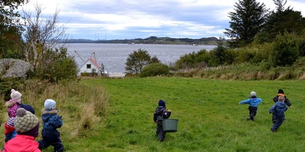 Barnehagebarn på en grønn slette eller svak hellende bakke, ned mot havet. 