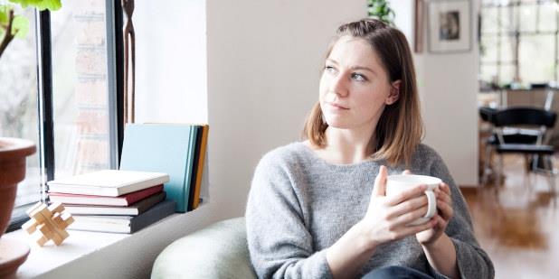 En ung kvinne sitter og holder med begge hendene rundt en kopp.