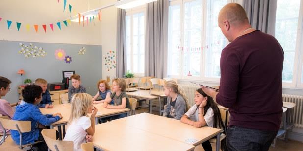 Foto av lærer som står foran elever og underviser i et klasserom