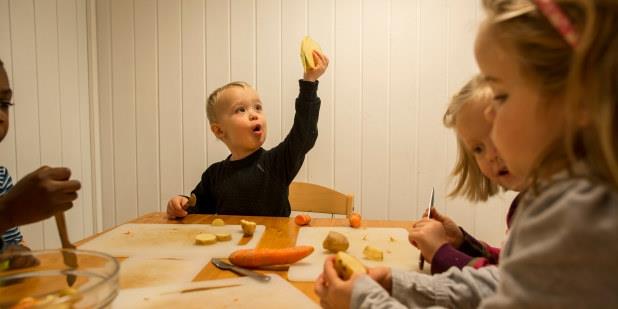 Barnehagebarn som sitter ved et bord og kutter opp grønnsaker. Foto.