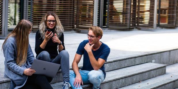 Foto av tre unge mennesker som smiler og prater i en trapp