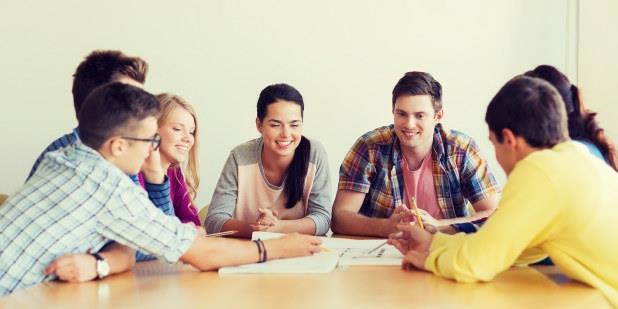 En gruppe studenter sitter rundt et bord mens de samtaler om dokumenter på bordet. Illustrasjonsfoto.