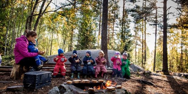 En barnehagelærer og sju barn rundt en bålplass i skogen. Foto.