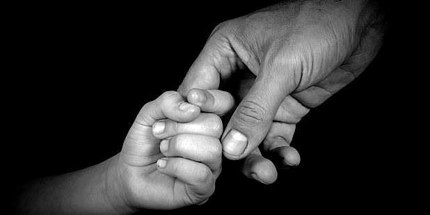 Bilde av en barnehånd som holder rundt pekefingeren til en voksenhånd. Bildet er i svart-hvitt.