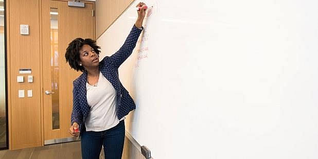 En svart kvinnelig lærer skriver på en tavle