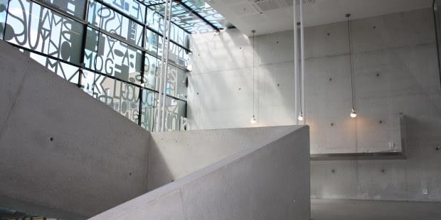 Trapp i betong og lys som skinner inn gjennom vindu med skrift. Foto.