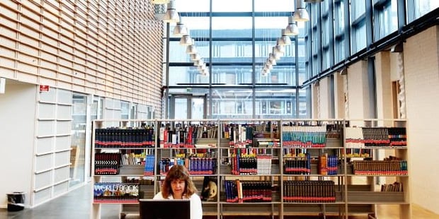 En person som sitter foran en PC i et bibliotek. Foto.