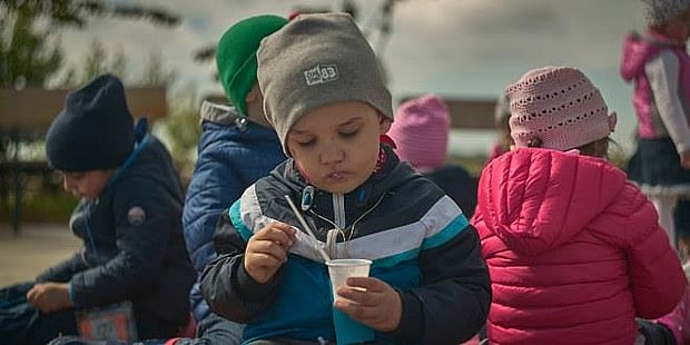 foto av barnehagegutt som spiser ute mens andre barn er i bakgrunnen