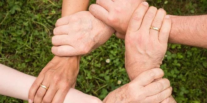 Seks hender som holder oppå neste persons arm. Hendene former en ring. 