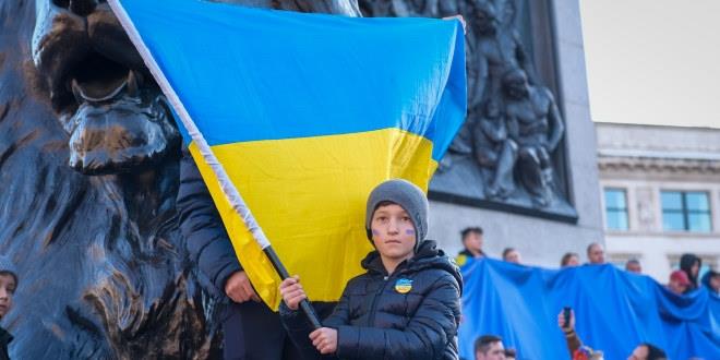 Et barn veiver det ukrainske flagget foran en statue. 