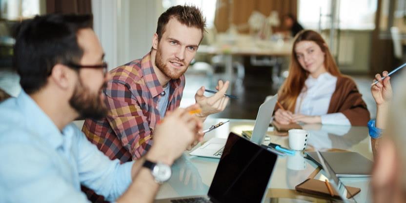 Tre voksne studenter rundt et bord i diskusjon