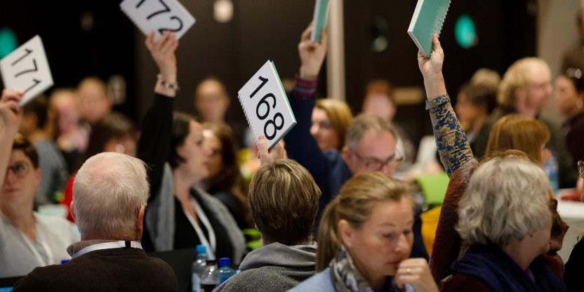 Bilde av mennesker som bruker delegatnummer-skilt til å stemme på et landsmøte.