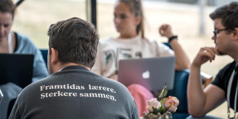 Fire mennesker rundt et bord. Rygg med tskjorte der det står "Framtidens lærere. Sterkere sammen." og front og i fokus. 