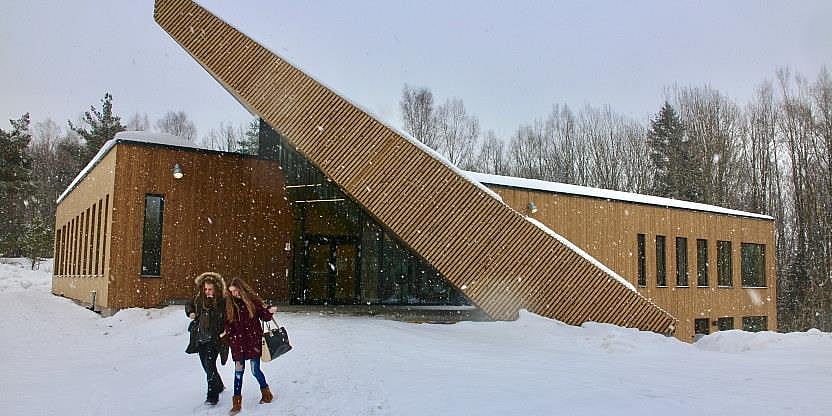 Bildet av et særpreget skolebygg i tre. Det er snøvær og to elever går fra skolen mot fotografen.